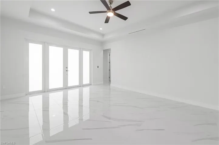 Spacious room featuring large format porcelain tile flooring, a tray ceiling with recessed lighting, and a modern ceiling fan