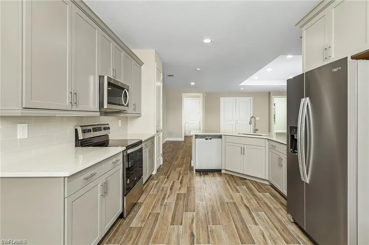 Kitchen with a tray ceiling, stainless steel appliances, light hardwood / wood-style floors, decorative backsplash, and sink