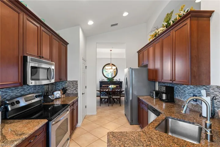 Kitchen with stainless steel appliances, backsplash, pendant lighting, vaulted ceiling, and light tile patterned flooring
