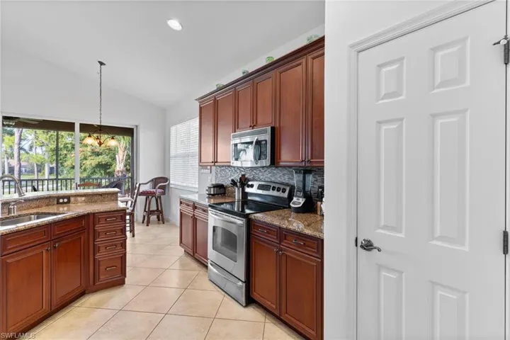 Kitchen featuring stainless steel appliances, pendant lighting, dark stone counters, lofted ceiling, and light tile patterned flooring