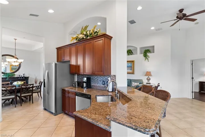 Kitchen featuring dark stone counters, a peninsula, a kitchen bar, decorative light fixtures, and ceiling fan
