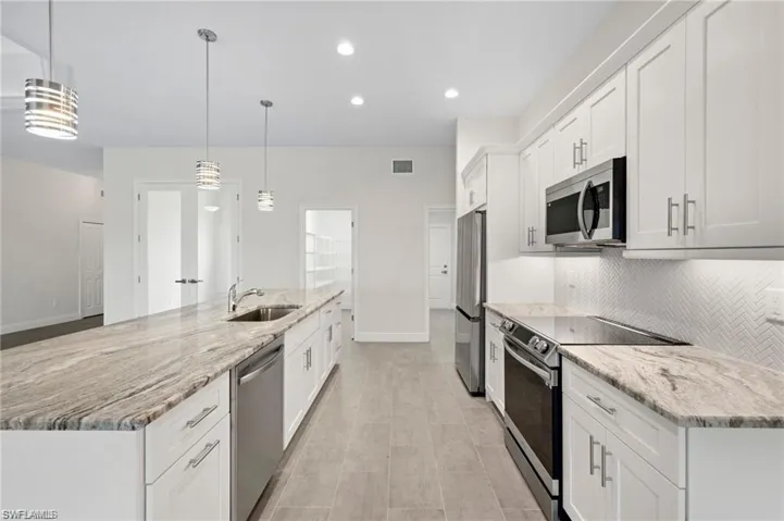 Kitchen with appliances with stainless steel finishes, white cabinetry, tasteful backsplash, a large island with sink, and light stone countertops