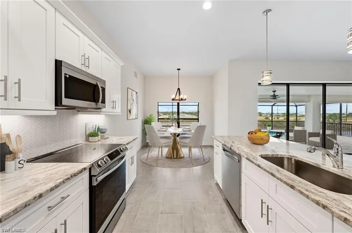 Kitchen with stainless steel appliances, backsplash, white cabinets, hanging light fixtures, and light stone counters