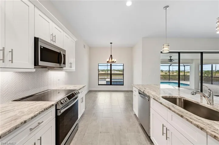 Kitchen featuring stainless steel appliances, backsplash, white cabinetry, decorative light fixtures, and light stone countertops