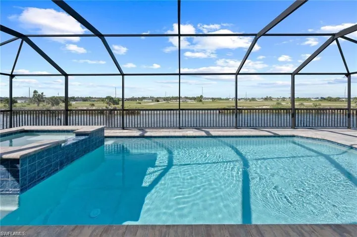 View of pool with a pool with connected hot tub, a water view, and glass enclosure