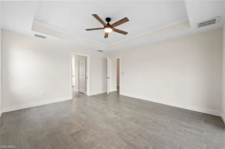 Empty room featuring a tray ceiling, a ceiling fan, and crown molding