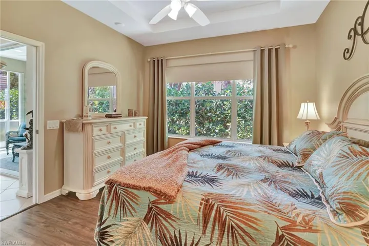Bedroom featuring a raised ceiling, access to exterior, wood finished floors, and ceiling fan