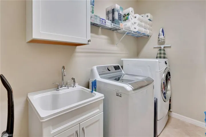 Laundry room featuring light tile patterned floors, baseboards, separate washer and dryer, a sink, and cabinet space