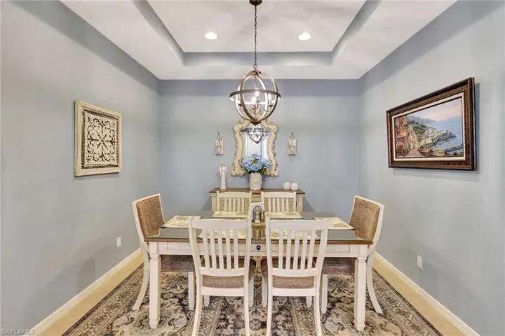 Dining space with a tray ceiling, baseboards, a chandelier, and wood finished floors