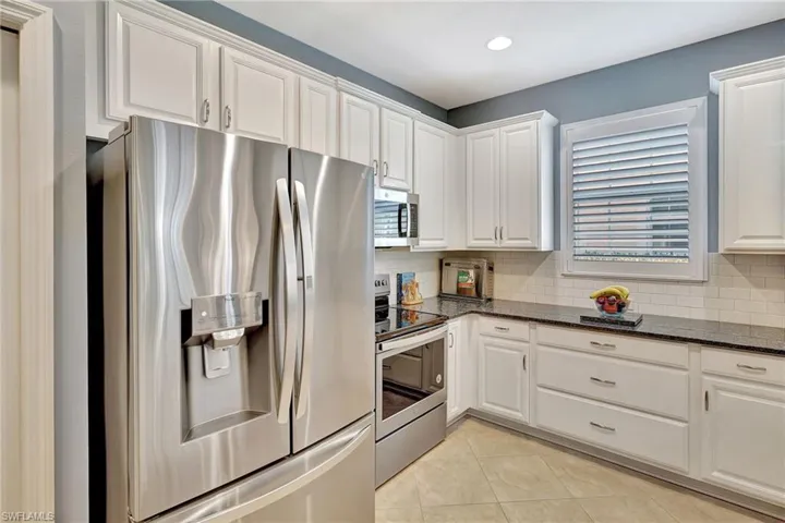 Kitchen with light tile patterned floors, backsplash, white cabinets, and stainless steel appliances