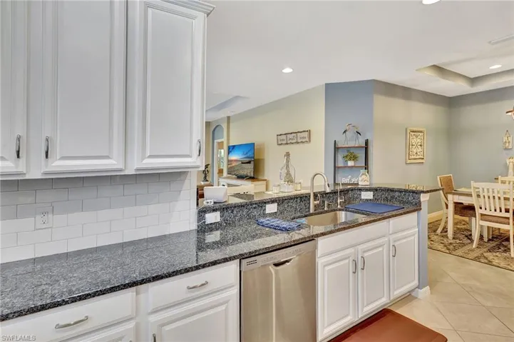 Kitchen featuring light tile patterned floors, white cabinets, a sink, backsplash, and stainless steel dishwasher