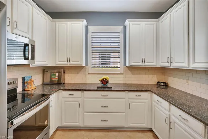 Kitchen with stainless steel appliances, white cabinetry, and backsplash