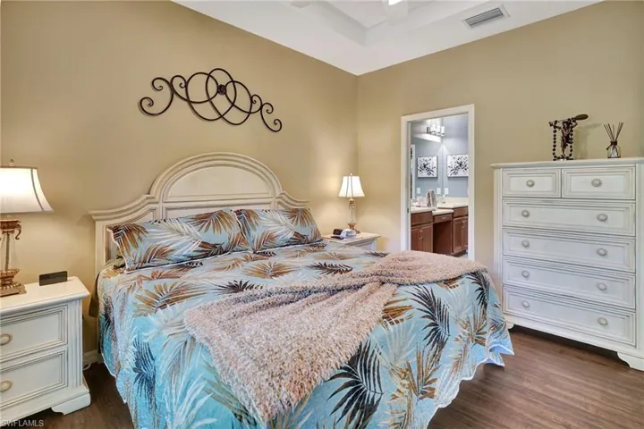 Bedroom with dark wood-style flooring, visible vents, and connected bathroom