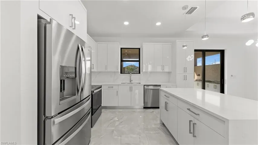 Kitchen featuring appliances with stainless steel finishes, light marble finish floors, decorative light fixtures, white cabinets, and recessed lighting