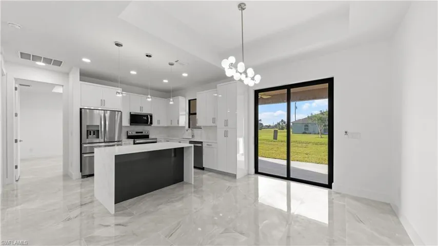 Kitchen with a center island, appliances with stainless steel finishes, white cabinets, pendant lighting, and a chandelier