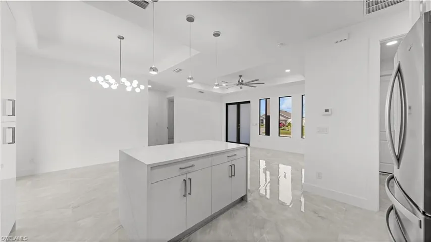 Kitchen with a tray ceiling, hanging light fixtures, freestanding refrigerator, a ceiling fan, and a kitchen island
