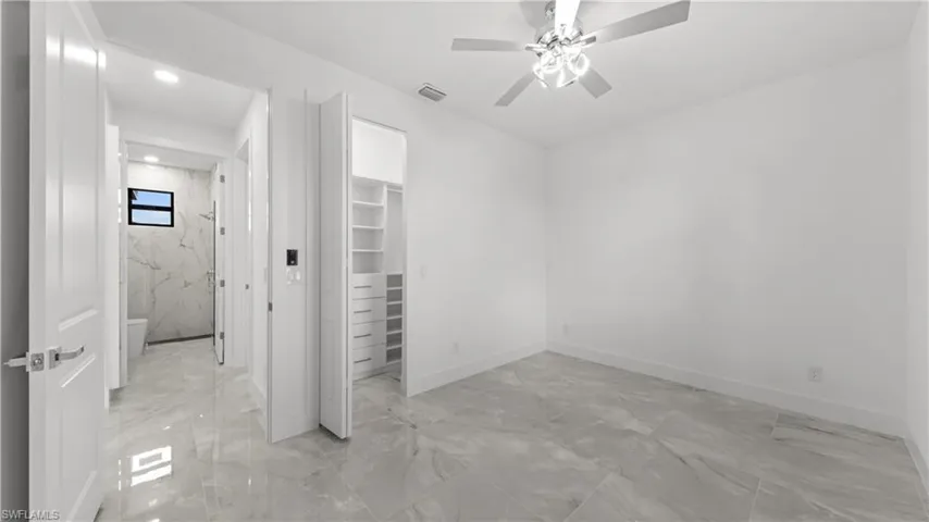 Unfurnished bedroom with light marble finish floors, a walk in closet, and ceiling fan