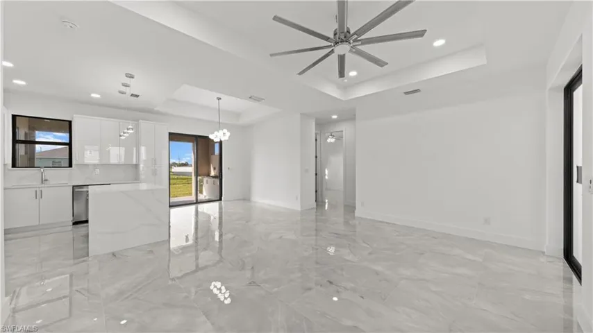 Spare room featuring a tray ceiling, light marble finish flooring, a chandelier, a ceiling fan, and recessed lighting