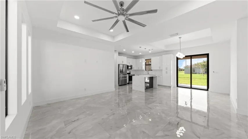 Unfurnished living room featuring a raised ceiling, light marble finish flooring, recessed lighting, and a ceiling fan