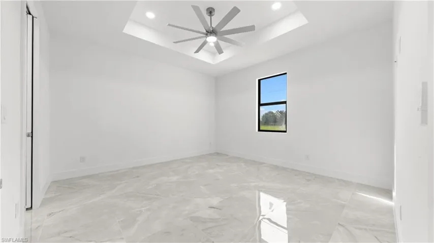 Spare room featuring a tray ceiling, recessed lighting, light marble finish flooring, and a ceiling fan