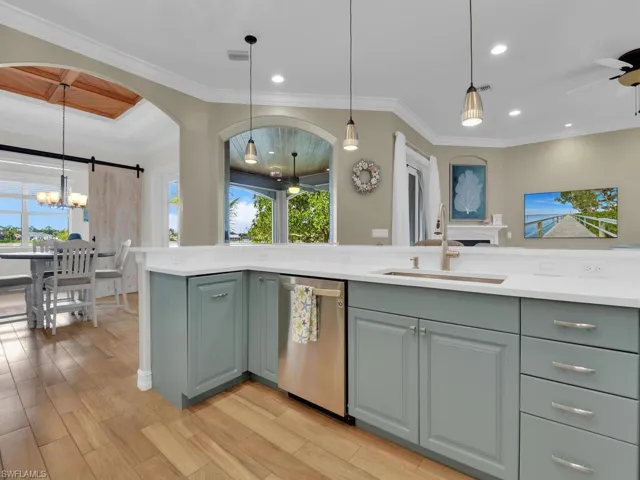 Kitchen with ornamental molding, ceiling fan with notable chandelier, sink, pendant lighting, and dishwasher