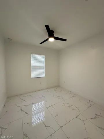 Empty room featuring light marble finish flooring and a ceiling fan