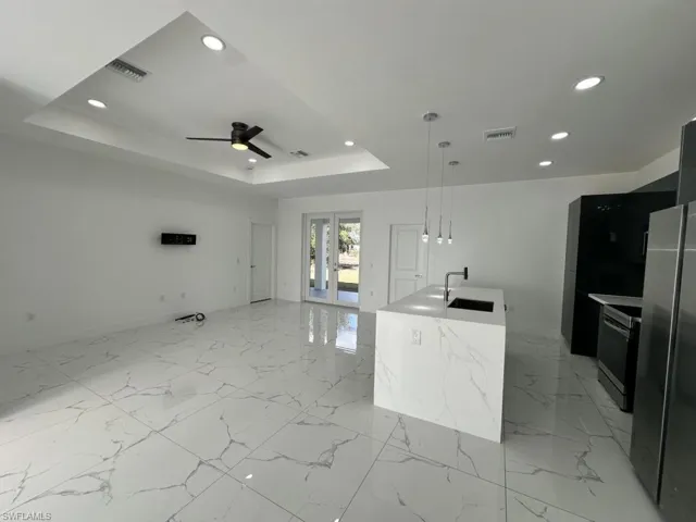 Kitchen featuring freestanding refrigerator, a kitchen island with sink, electric range oven, hanging light fixtures, and a ceiling fan
