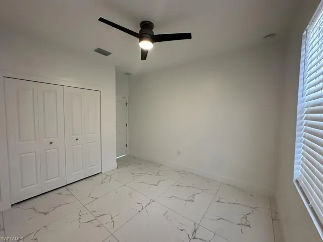 Unfurnished bedroom featuring ceiling fan, light marble finish flooring, and a closet