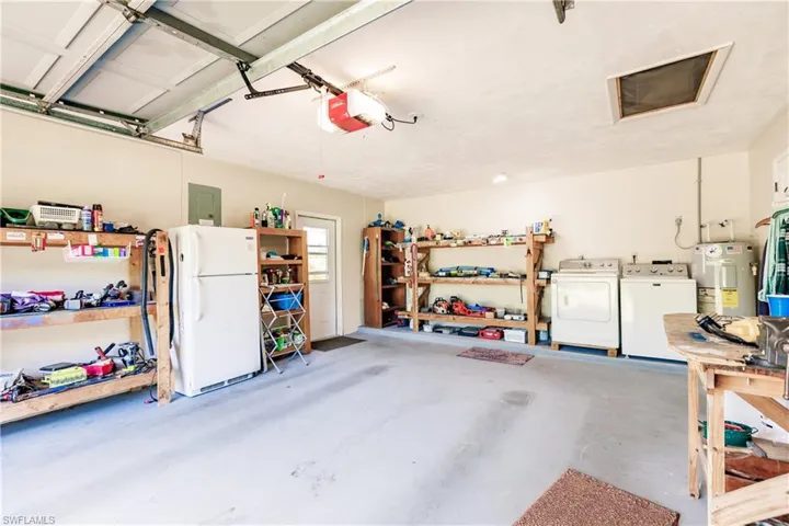 Garage with electric panel, a garage door opener, electric water heater, washing machine and dryer, and white refrigerator