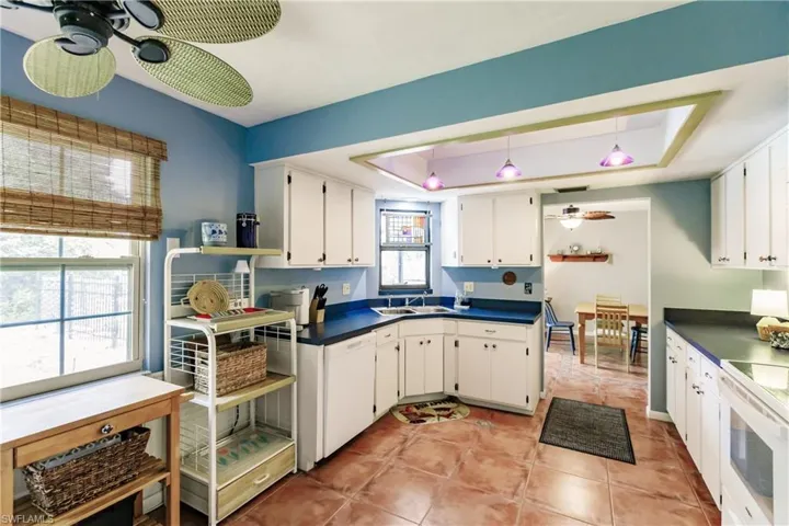 Kitchen featuring light tile patterned flooring, white appliances, white cabinets, a tray ceiling, and ceiling fan