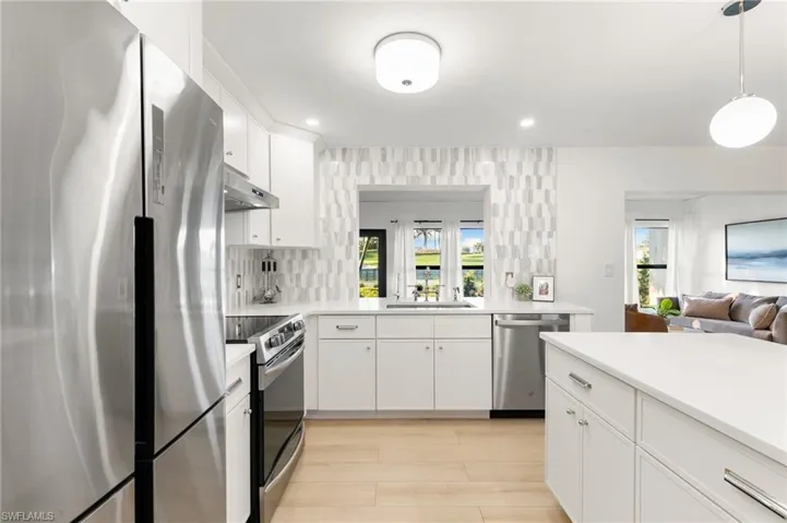 Kitchen featuring under cabinet range hood, appliances with stainless steel finishes, light countertops, and a sink