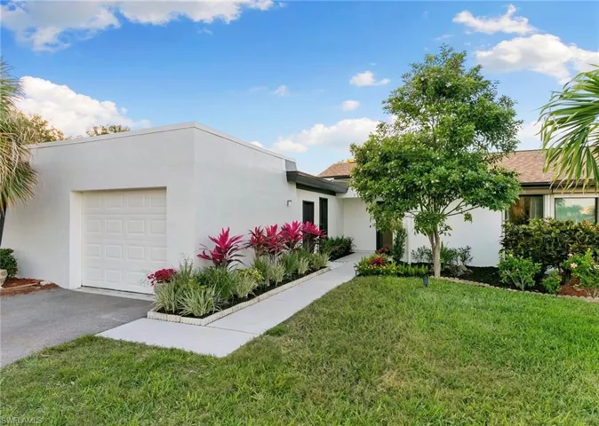View of front of house with an attached garage, driveway, a front lawn, and stucco siding