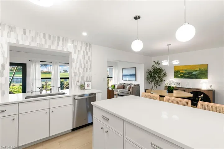 Kitchen featuring open floor plan, light countertops, stainless steel dishwasher, white cabinetry, and a sink