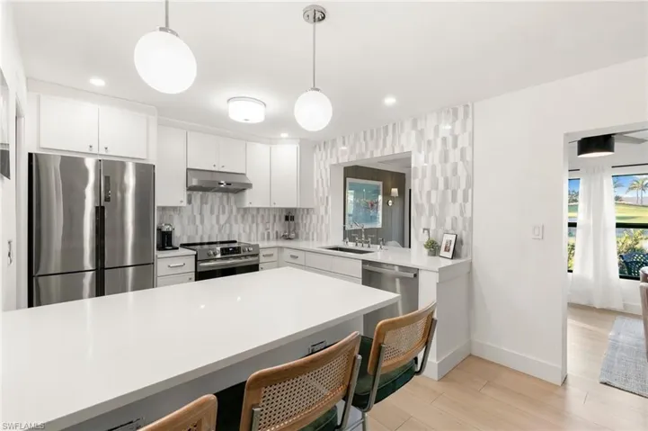 Kitchen featuring stainless steel appliances, light countertops, a sink, under cabinet range hood, and a kitchen bar