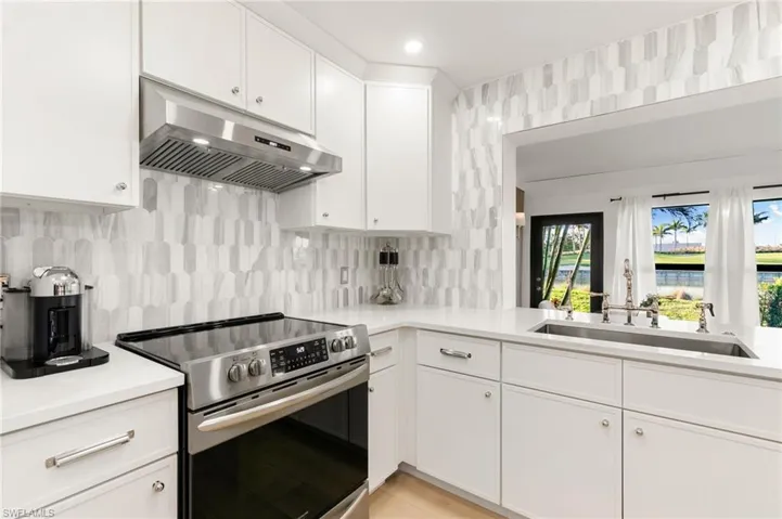 Kitchen featuring under cabinet range hood, a sink, light countertops, decorative backsplash, and stainless steel electric range oven