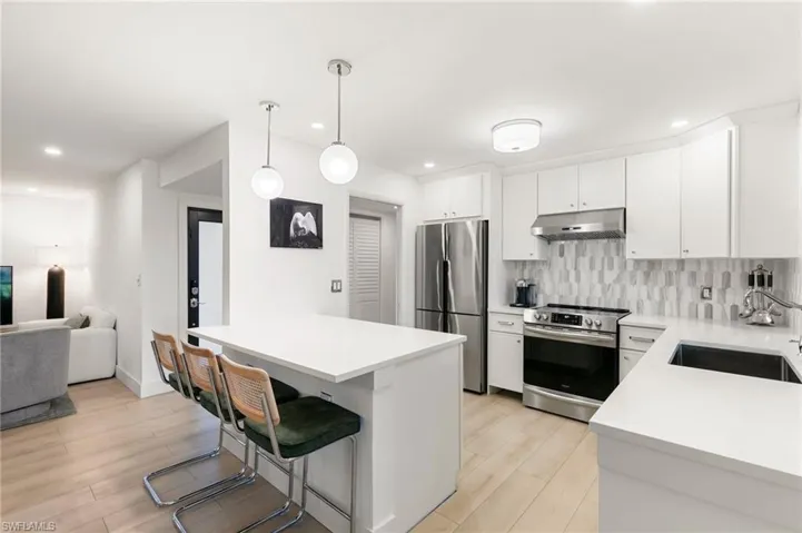 Kitchen featuring decorative backsplash, a kitchen breakfast bar, stainless steel appliances, under cabinet range hood, and a sink