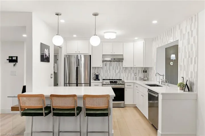 Kitchen with appliances with stainless steel finishes, a sink, light countertops, under cabinet range hood, and backsplash