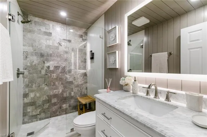 Bathroom featuring wooden ceiling, toilet, vanity, tile walls, and a stall shower