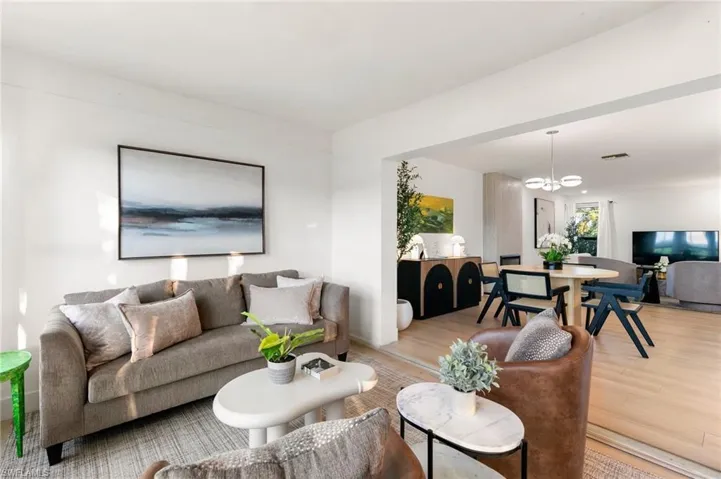 Living area featuring light wood-type flooring, visible vents, and an inviting chandelier