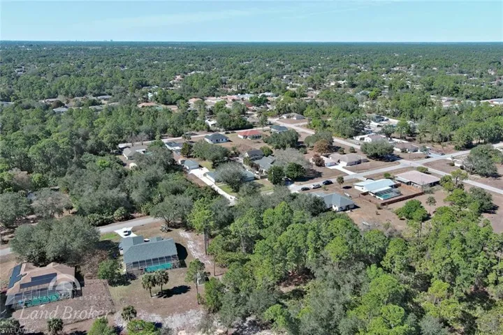 Aerial view of property and surrounding area featuring a forest and nearby suburban area