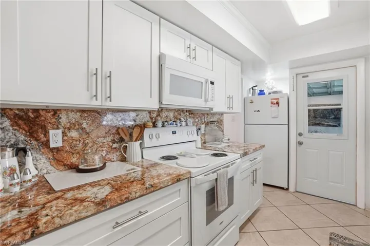 Kitchen with white appliances, white cabinetry, backsplash, ornamental molding, and light tile patterned flooring