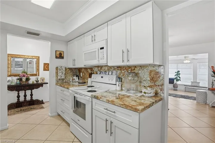 Kitchen featuring white appliances, white cabinetry, light tile patterned flooring, crown molding, and decorative backsplash