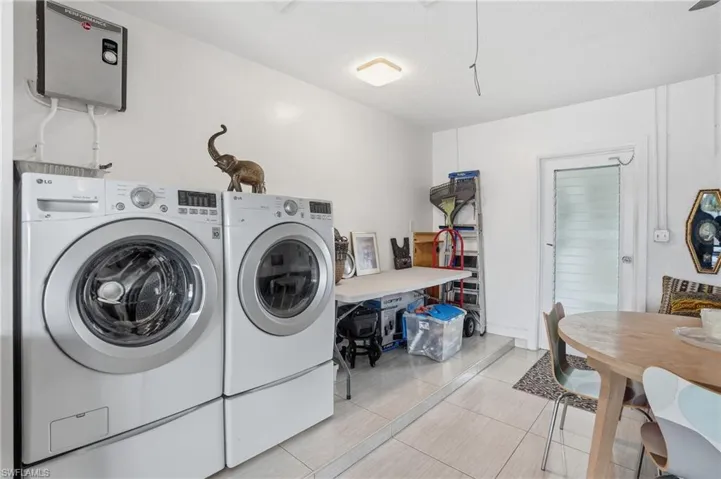 Laundry area featuring water heater, washer and clothes dryer, and light tile patterned floors