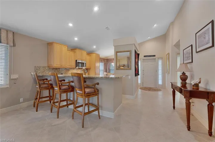 Kitchen with kitchen peninsula, a healthy amount of sunlight, light stone counters, and light brown cabinetry