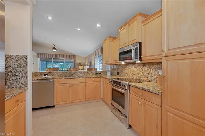 Kitchen with sink, vaulted ceiling, light tile patterned floors, light brown cabinetry, and appliances with stainless steel finishes