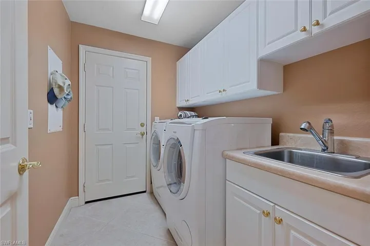 Clothes washing area with cabinets, sink, washer and clothes dryer, and light tile patterned floors