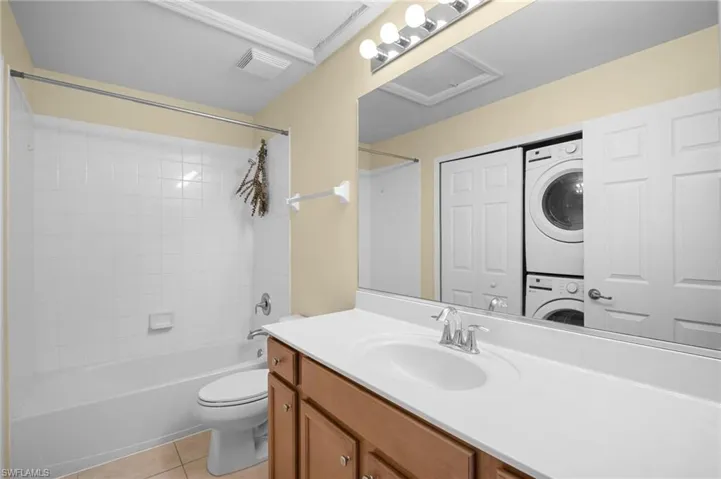 Bathroom with vanity, bathtub / shower combination, stacked washer and dryer, and light tile patterned floors