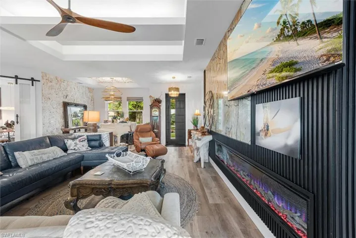 Living area featuring wood-finish flooring, a tray ceiling, and a prominent feature wall with vertical paneling and an integrated linear electric fireplace