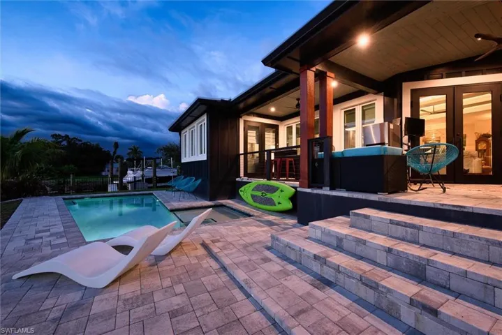 Exterior patio featuring a rectangular swimming pool, paver decking, multi-level stairs, and a covered porch with exposed wood beams