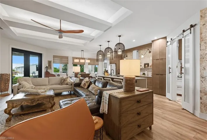 Open-concept living space featuring wood-finish flooring, a coffered ceiling with a modern fan, and double French doors